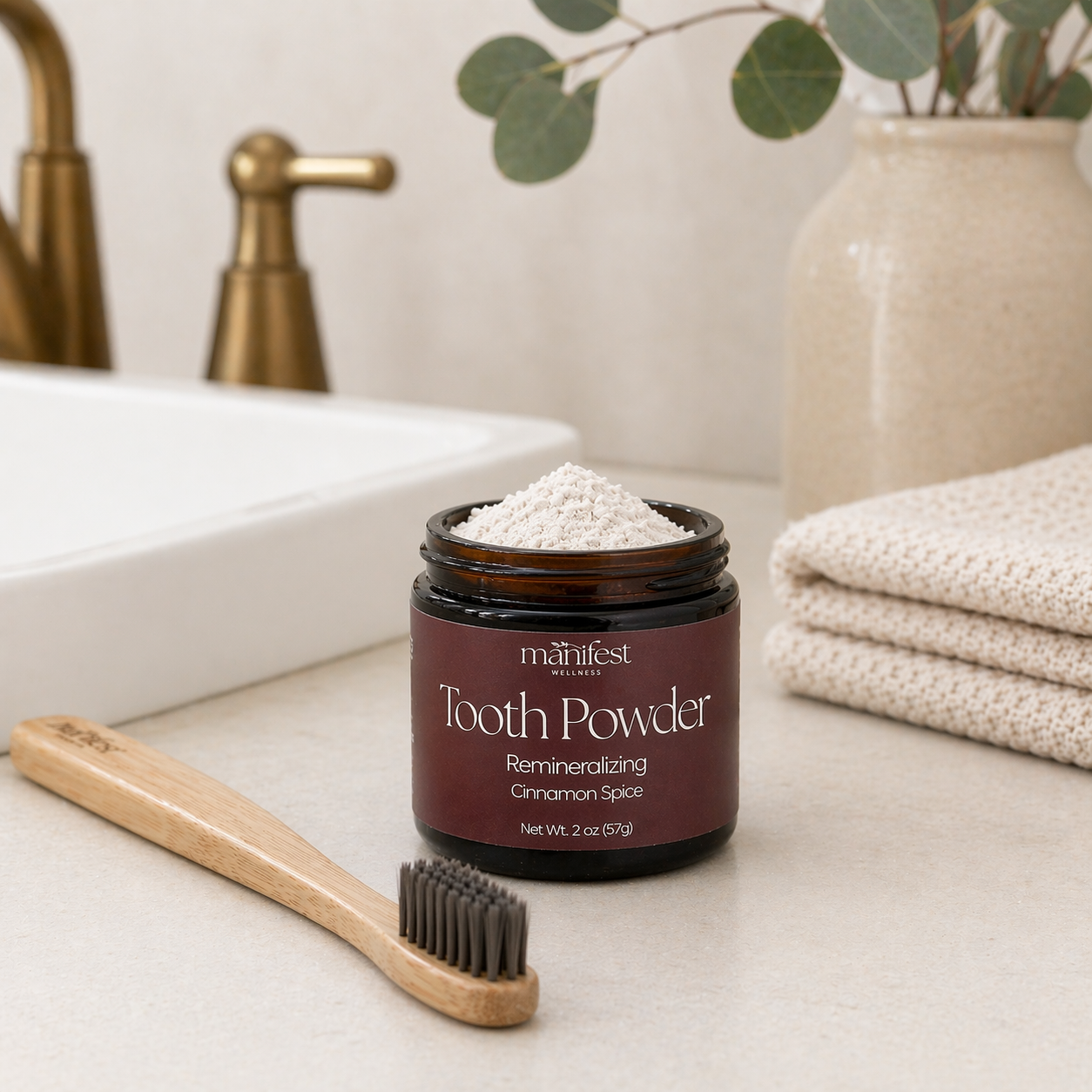 Jar of Manifest Wellness Cinnamon Spice Tooth Powder on a bathroom counter with a bamboo toothbrush.