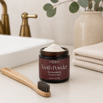 Jar of Manifest Wellness Cinnamon Spice Tooth Powder on a bathroom counter with a bamboo toothbrush.