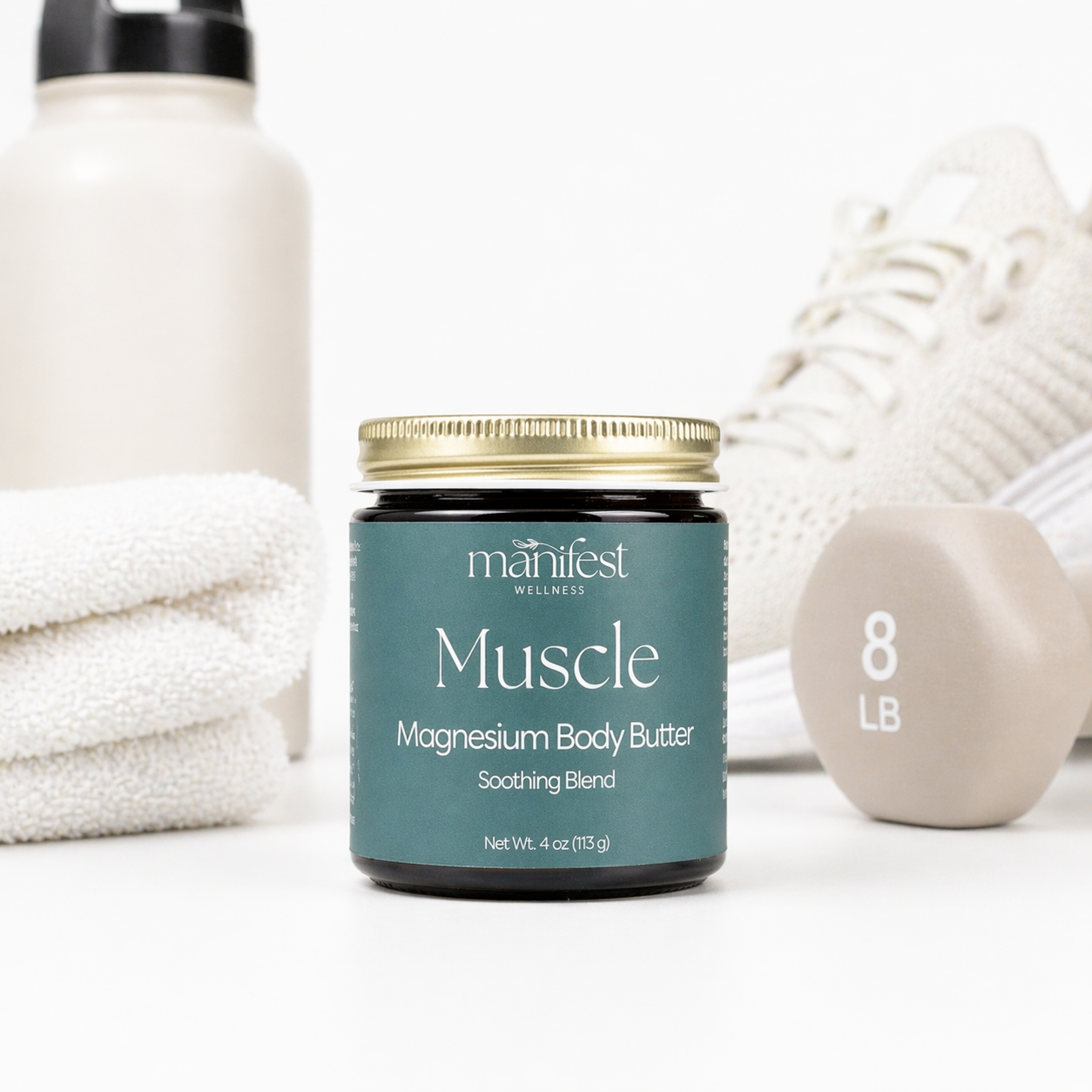 Manifest Wellness Muscle Magnesium Body Butter jar on a white surface with towels and a ball in the background