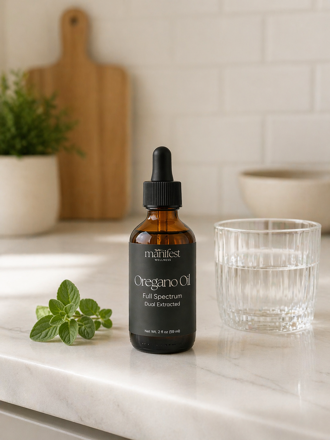 Bottle of Manifest Wellness Oregano Oil on a kitchen counter with a glass and herbs in the background