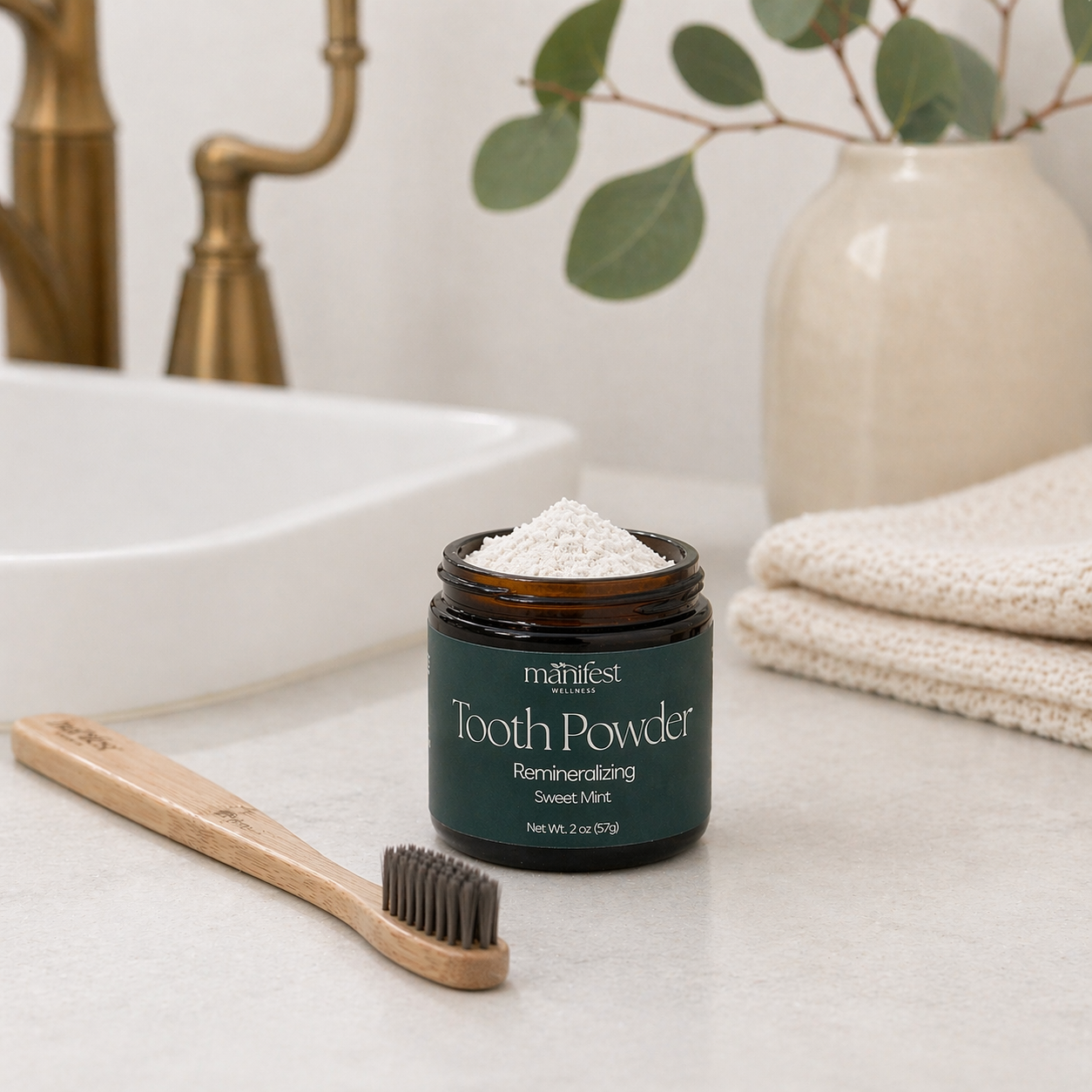 Jar of Manifest Wellness Tooth Powder on a bathroom counter with a bamboo toothbrush.