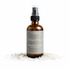 Brown spray bottle labeled Unscented Magnesium Spray by manifest wellness on a white background with magnesium chloride flakes.