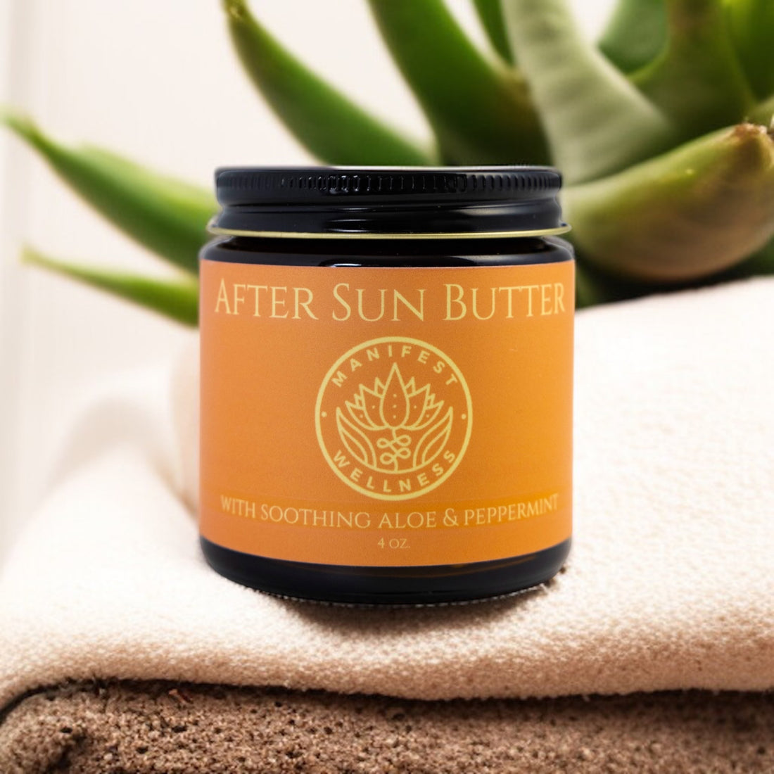 A glass jar of After Sun Butter with Aloe, Peppermint, Lavender, and Tea Tree, placed on a towel next to an aloe plant.