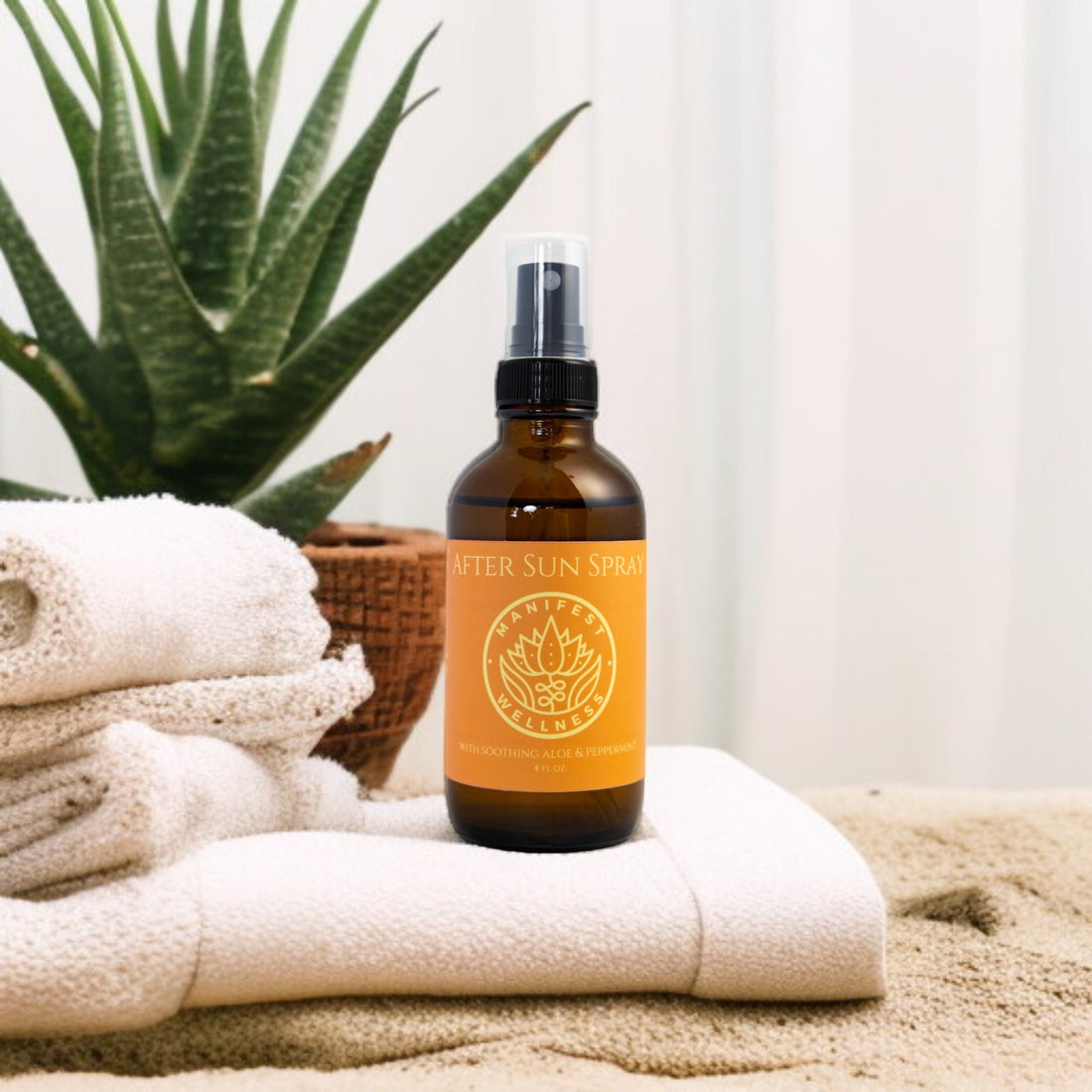 A bottle of After Sun Spray in a glass bottle with Aloe, Peppermint, Lavender and Tea Tree, placed on a sandy surface with a white towel and a potted aloe plant in the background.