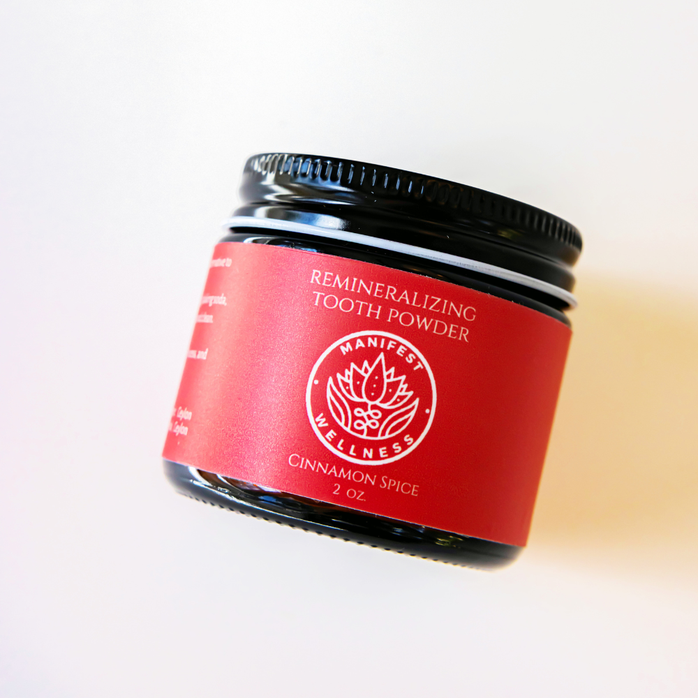 A glass jar with a black metal lid and a red label of Remineralizing tooth powder, cinnamon spice with a white background.
