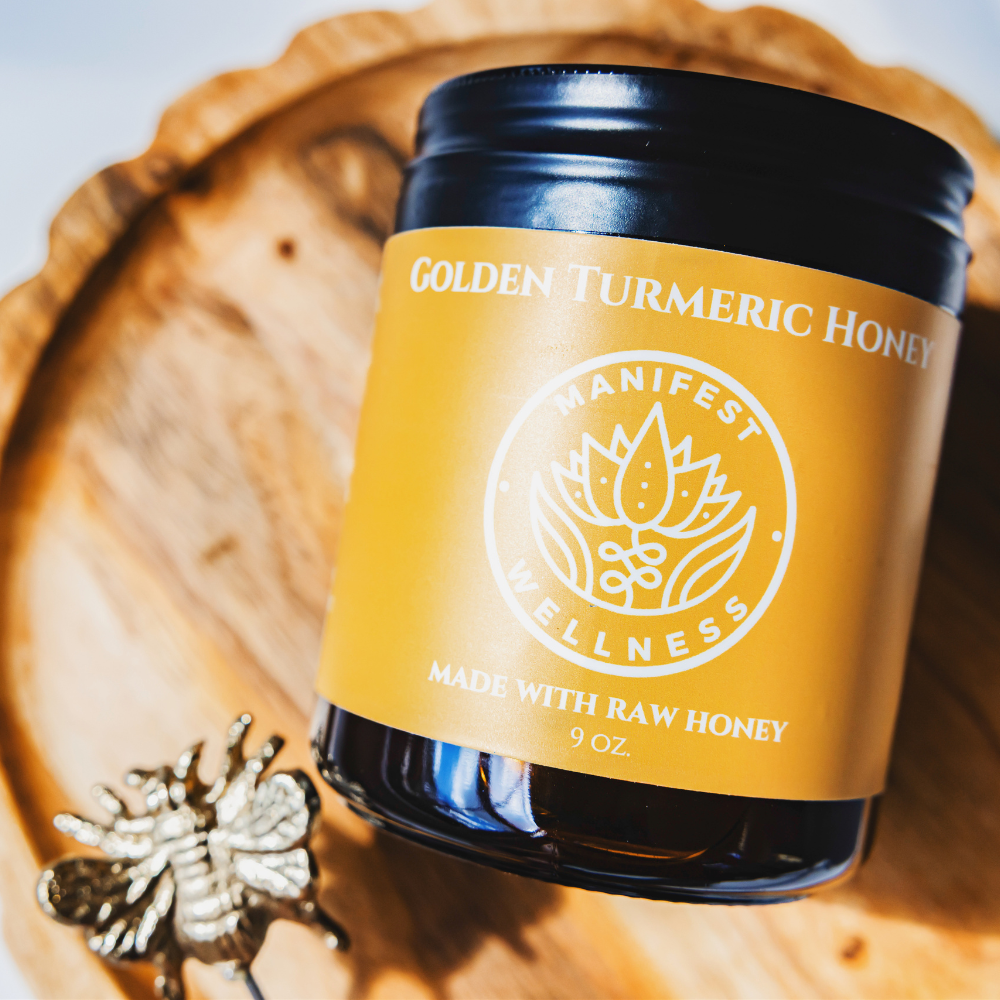 A glass jar with a black metal lid and a yellow label of golden honey laying on a round wood stand with a gold honey bee on a stick