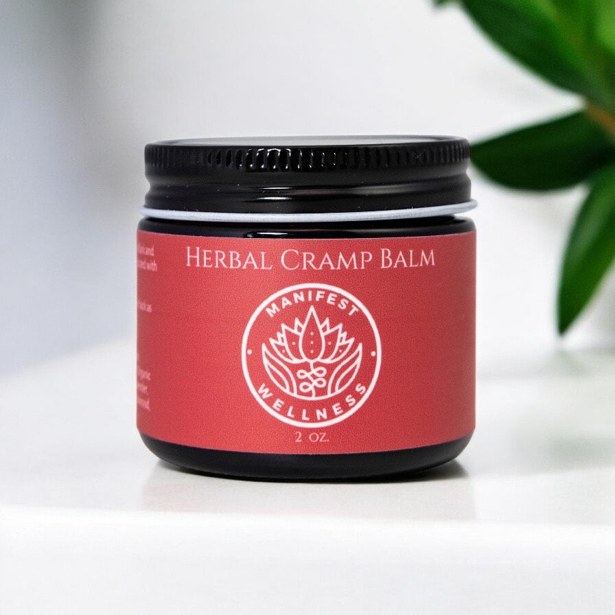 A 2oz amber glass jar of Herbal Cramp Balm with a red label that includes the product name and the brand &