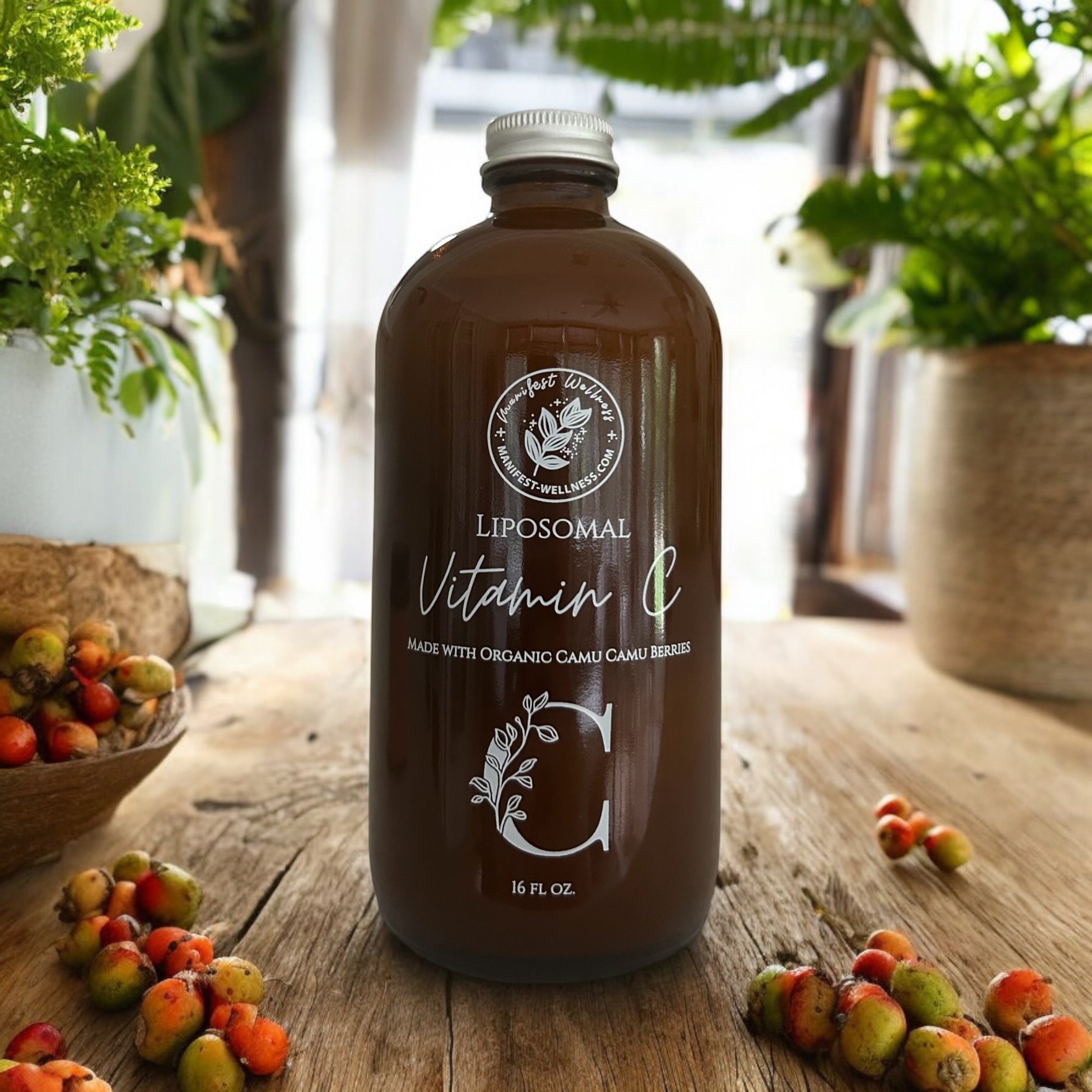A bottle of liposomal vitamin C supplement in an amber bottle with white writing on a wooden surface with camu camu berries scattered around, and plants in the background.