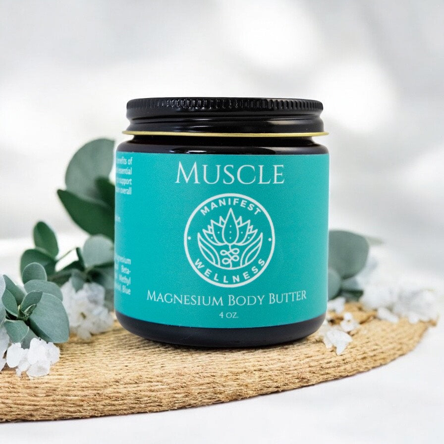 A glass jar of Muscle Magnesium Body Butter from Manifest Wellness on a white background with greenery.