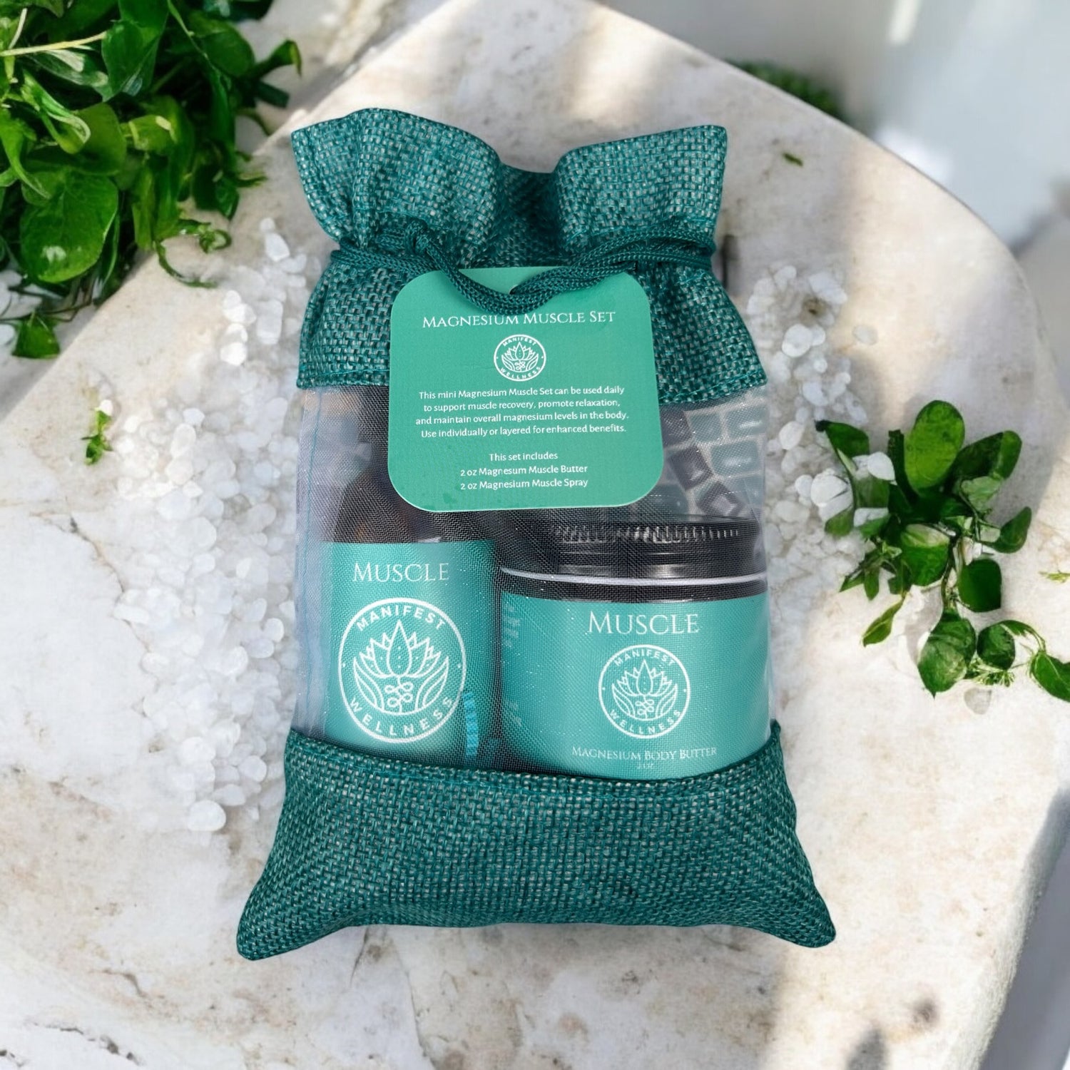A gift set of Magnesium Muscle Spray and Butter in 2oz glass spray and jar. Products are in a blue fiber bag laying on a table with herbs and magnesium chloride around.