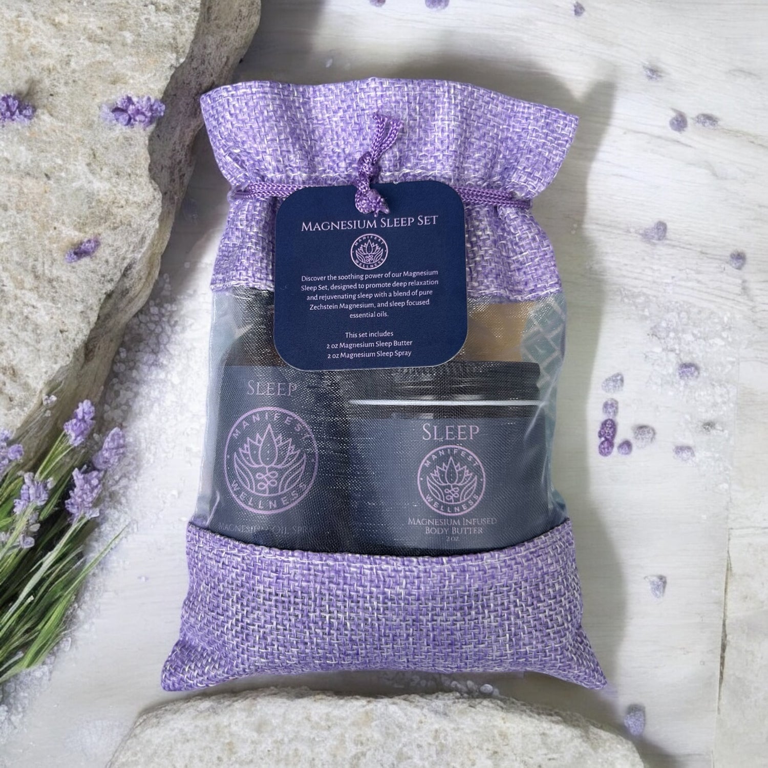 A gift set with a blue tag that reads magnesium sleep set inside a purple natural fiber bag with two bottles inside. On a light background with lavender and purple stones around.