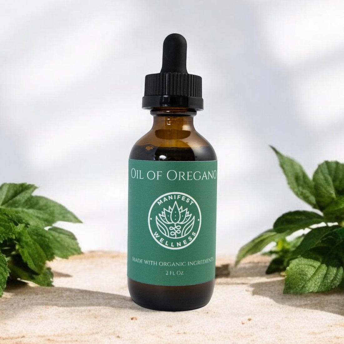 A glass bottle of Oil of Oregano from Manifest Wellness with green label and black dropper with a light background and oregano leaves around.