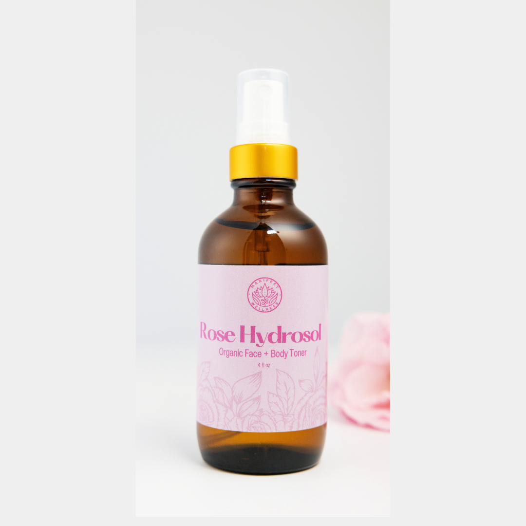 A glass bottle of Rose Hydrosol with a spray nozzle, displayed against a white background with a pink rose to the side.